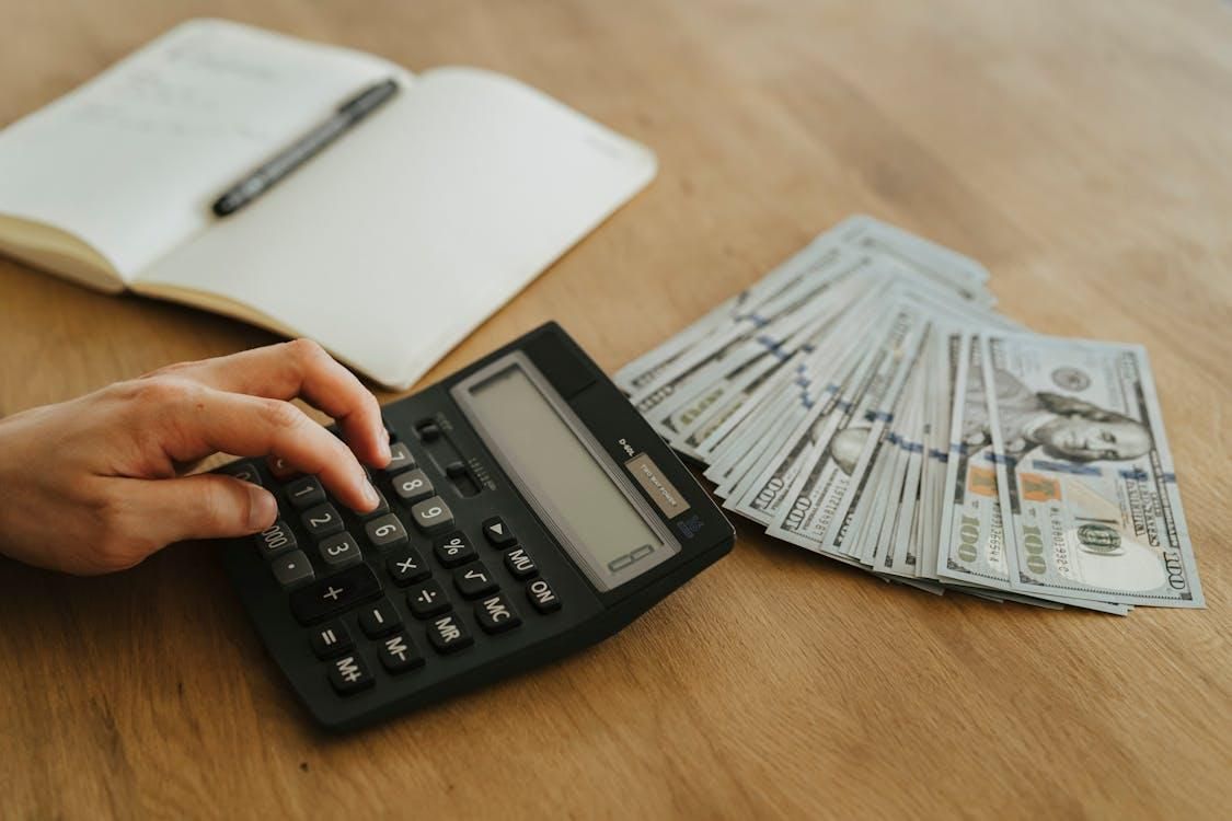 A calculator, money, and a daily planner on a wooden desk.